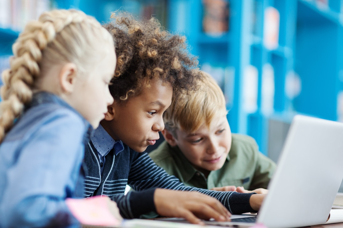 Three elementary students using a laptop together in a classroom